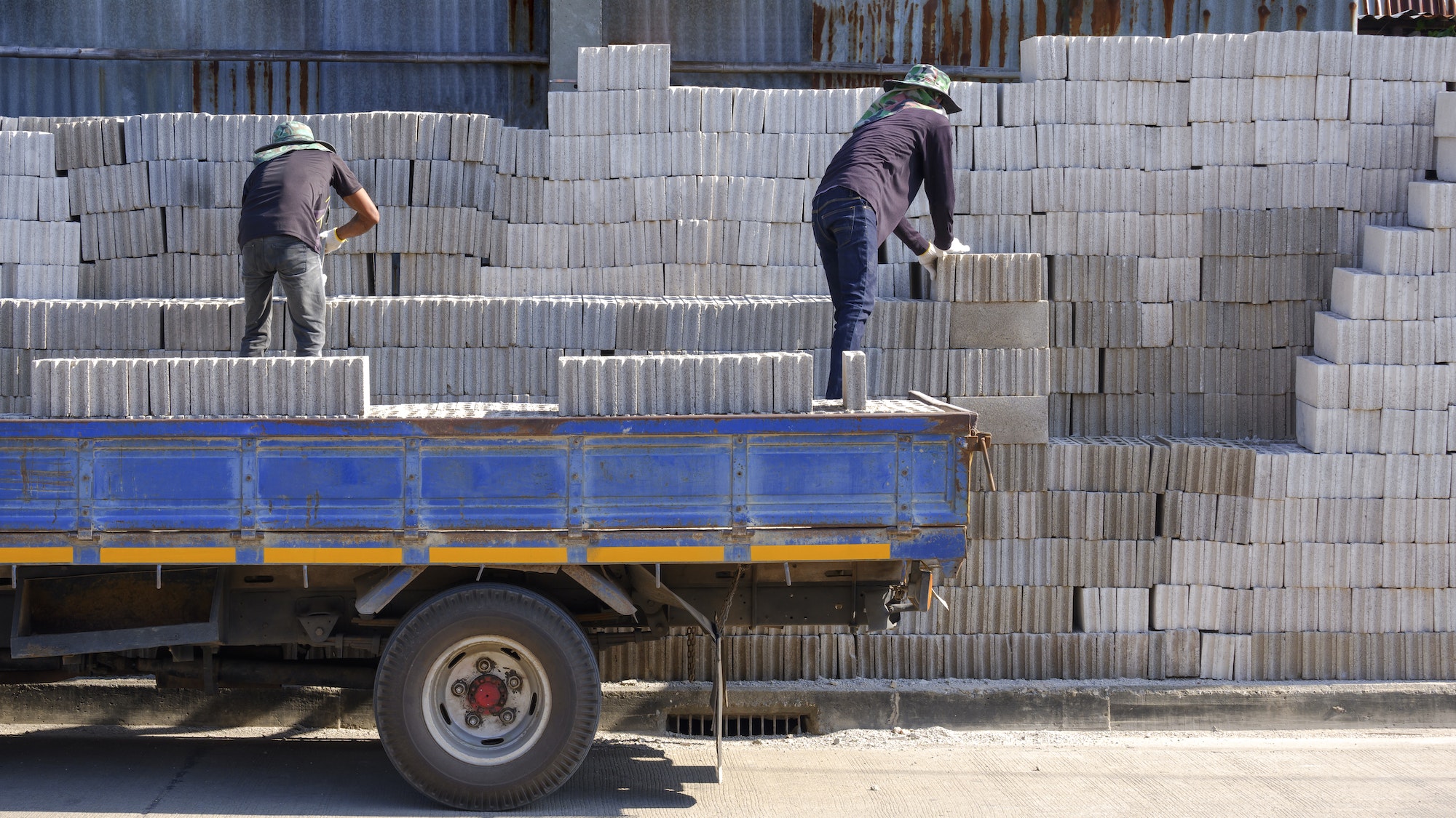Rear view of 2 Asian workers are loading concrete blocks into the truck for delivery to customers